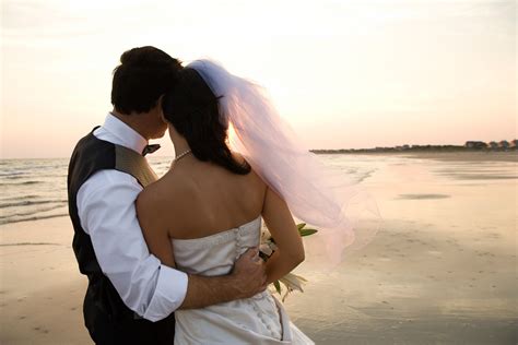 Newlywed Couple on Beach - Rear view of a newlywed couple hugging on beach. Horizontal shot ...