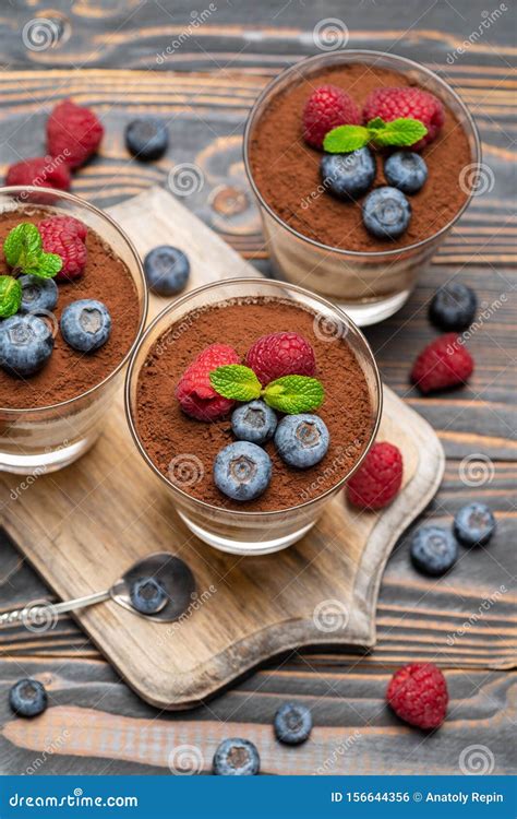 classic tiramisu dessert with blueberries and strawberries in a glass cup on cutting board on