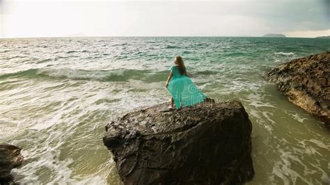woman walks on rock of sea reef stone stormy cloudy ocean blue swimsuit dress tunic concept