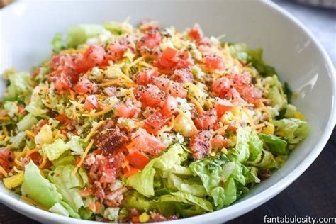 A White Bowl Filled With Lettuce Tomatoes And Other Toppings On Top Of It