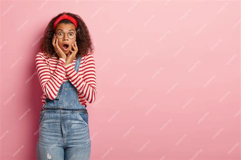 Шокированная девочка подросток позирует в комбинезоне с вьющимися волосами Бесплатно Фото