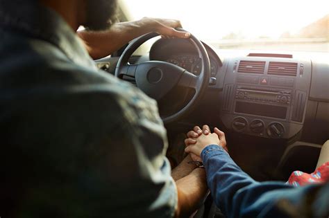 Close Up Of Couple Holding Hands Inside Car Driving On Mountain Road