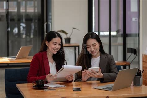 Two Asian Female Colleagues Sitting Next To Each Other In An Office