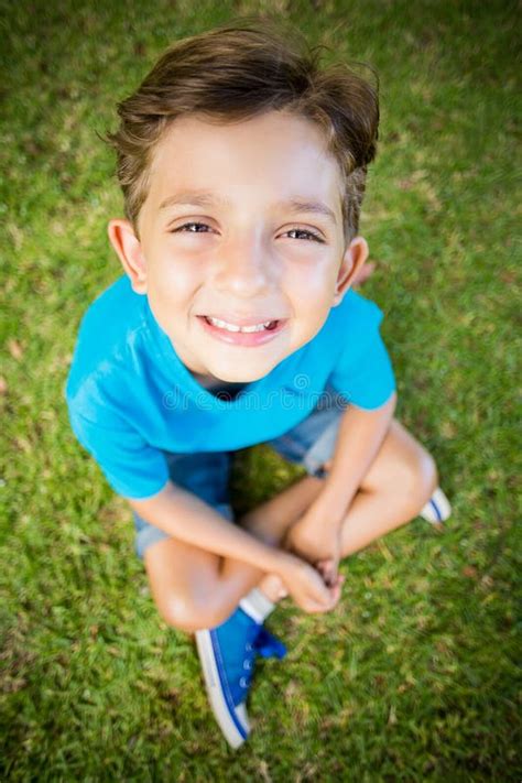 Young Boy Sitting On Grass And Smiling At Camera In Park Stock Image