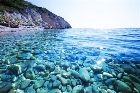 Seascape Of Still Blue Sea Waters Shore Stone Beach And Green Rock