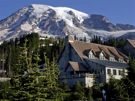 A Large House In Front Of A Mountain With Snow On Its Top And Trees