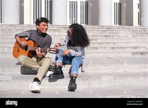 A Young Latin Couple Playing The Guitar And Singing Sitting On Stairs