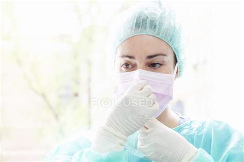 Close Up Of Female Nurse Wearing Surgical Mask Against Window In