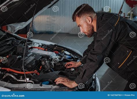 A Young Mechanic Is Very Focused On Looking At The Engine Of The Car He