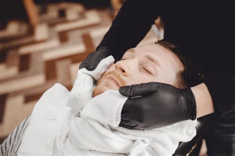 man sits in barbershop chair and steam his face with hot towel in front of royal beard shaving