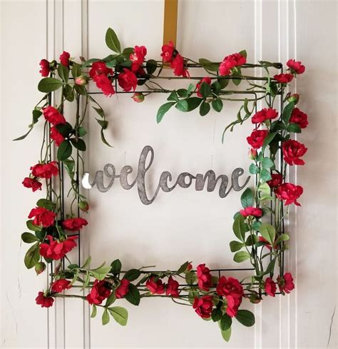 A Welcome Sign Made Out Of Metal Letters And Red Flowers On A White