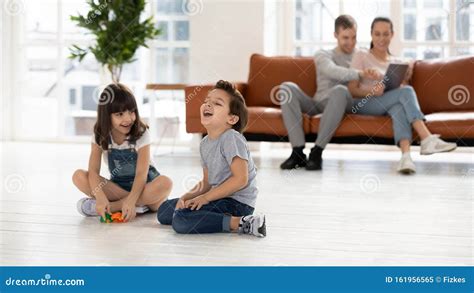 Cheerful Siblings Playing With Toys Together Parents Sit On Couch