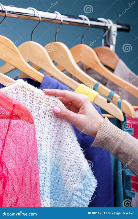 Female Hand Selects Colorful Clothes On Wood Hangers On Rack In Stock