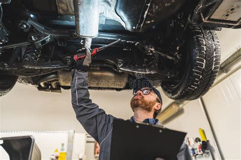 Mechanic With A Clipboard Inspecting Car Chassis Of A Lifted Car Using