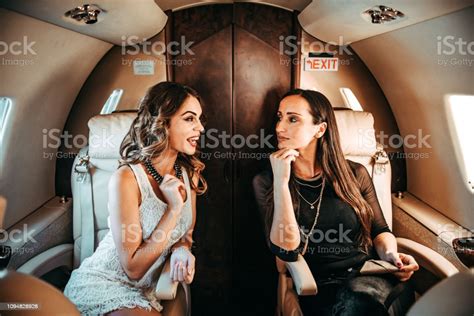 two rich glamorous women talking while sitting side by side aboard a private jet on a business