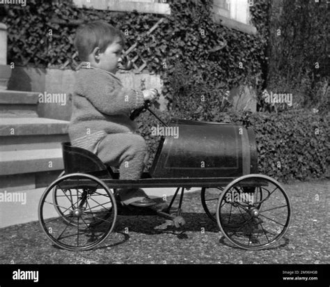 A Little Boy Riding Along In A Toy Car With A Pipe In His Mouth Stock