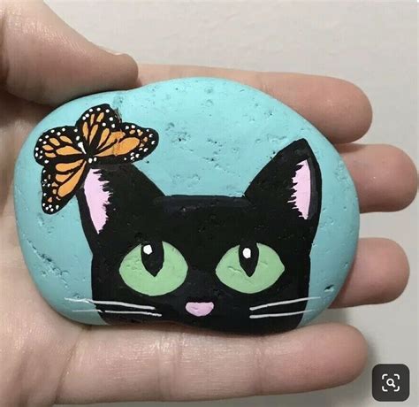 A Hand Holding A Painted Rock With A Black Cat And Butterfly On Its Head