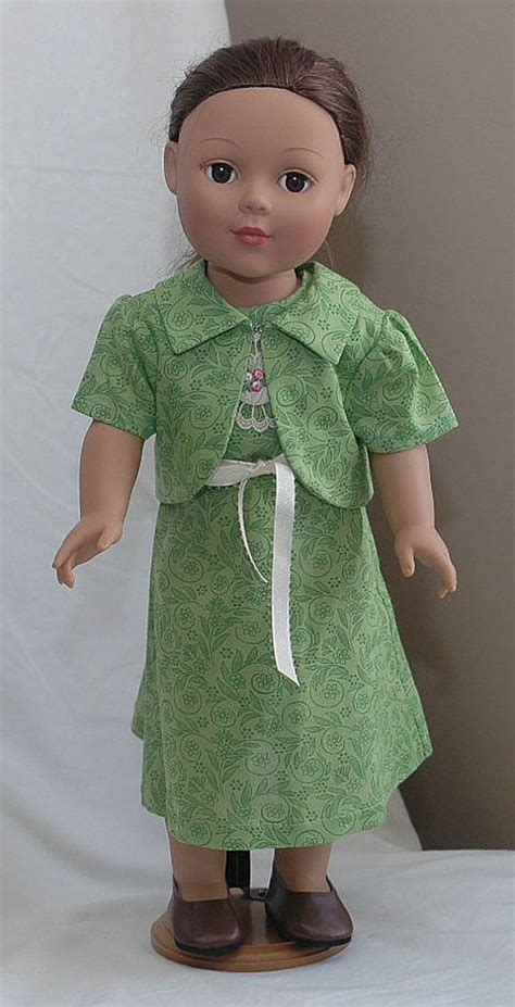 The Doll Is Wearing A Green Dress And Brown Shoes With A White Ribbon