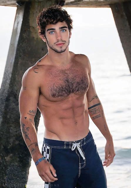 A Shirtless Man Standing Under A Pier Next To The Ocean With Tattoos On