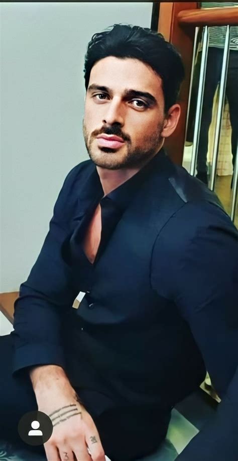 A Man In A Black Shirt And Tie Sitting Down