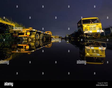 Trucks Parked On Each Side Of The Road Seen Reflected On A Large Puddle