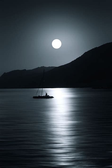 A Boat Floating On Top Of A Large Body Of Water Under A Moon Filled Sky