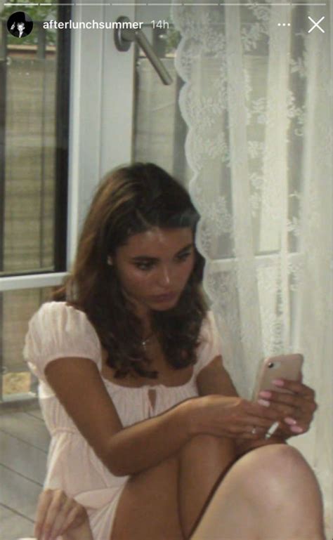 A Woman Sitting On The Floor Looking At Her Cell Phone While She S Holding Something In Her Hand