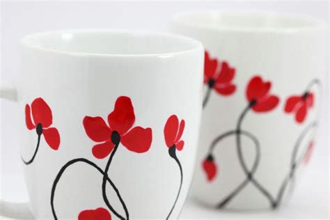 Two White Coffee Mugs With Red Flowers Painted On The Sides And Black