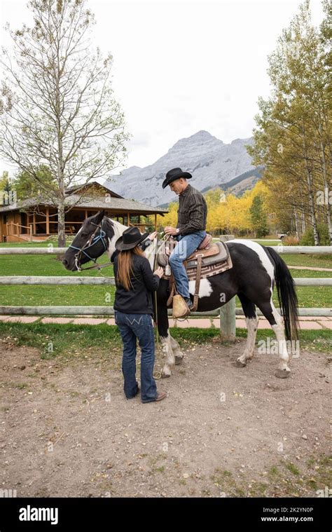 Female Rancher Helping Man Prepare For Horseback Riding On Ranch Stock