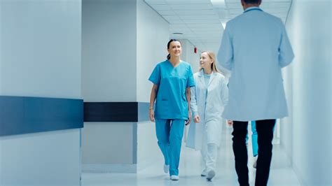 Female Surgeon And Female Doctor Walk Through Hospital Hallway Talking