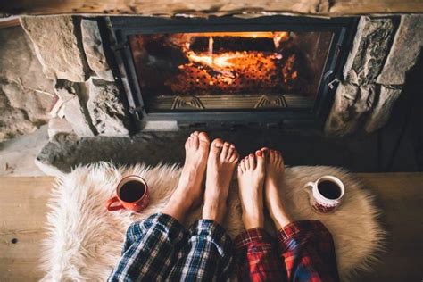 two people sitting in front of a fireplace with their feet up on the floor next to each other