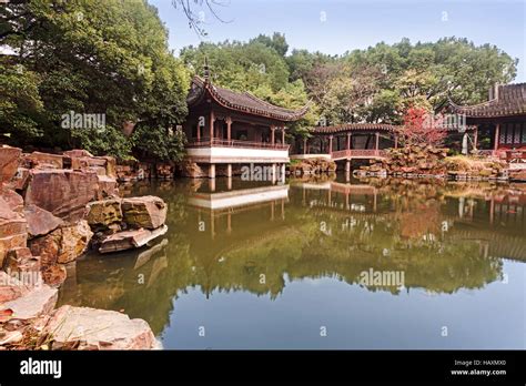Traditional Chinese Pavilion Bridge And House Reflecting In Still Water Of Quiet Pond Within