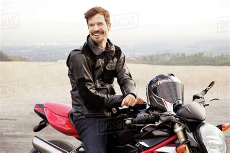 Cheerful Biker Sitting On Motorcycle At Countryside Stock Photo
