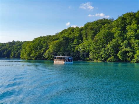 Tourist Boat Cruises Along Emerald Lake In Plitvice Surrounded By Lush