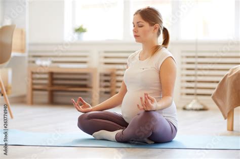 Full Length Portrait Of Pregnant Woman Sitting In Lotus Position While