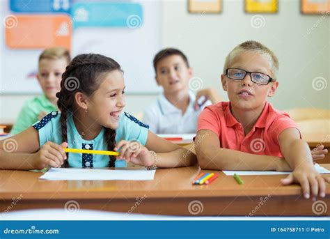 Happy Elementary Students Sitting At Desk And Joyful Discussing In