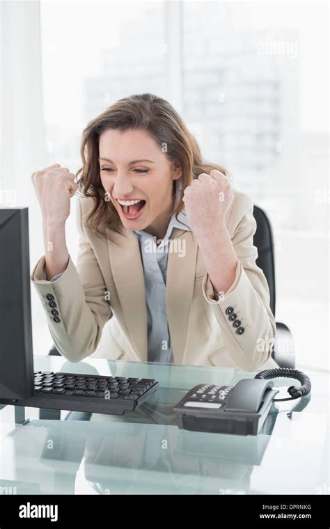 Businesswoman Cheering With Clenched Fists At Office Desk Stock Photo