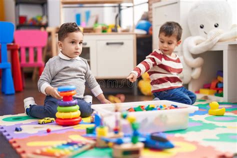 Two Kids Playing With Toys Sitting On Floor At Kindergarten Stock Photo