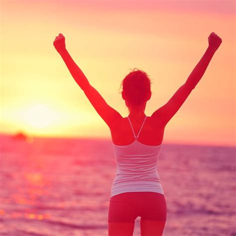A Woman Standing On The Beach At Sunset With Her Arms In The Air