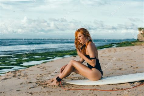 Joven hermosa niña posando en la playa con una tabla de surf surfista