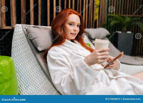 Portrait Of Redhead Young Woman Wearing Bathrobe Relaxing With Smartphone Lying On Lounger By
