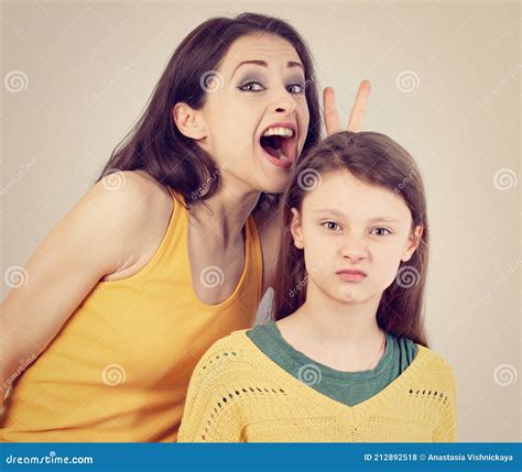 happy laughing crazy mother showing the horns above her daughter head with angry unhappy face
