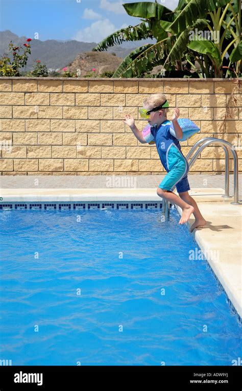 Young Boy Jumping Into Swimming Pool On Sunny Vacation Or Holiday Stock