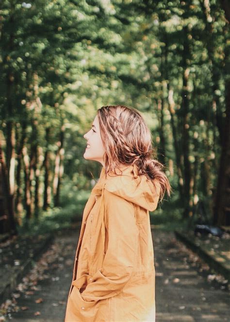 A Woman Standing In The Middle Of A Forest With Her Arms Around Her