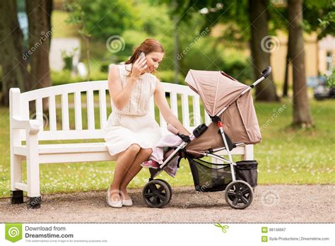 Happy Mother With Smartphone And Stroller At Park Stock