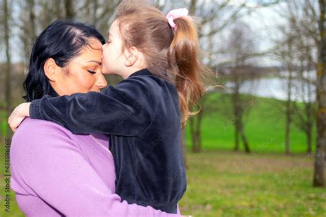 beautiful mother and daughter kissing to forehead hugs in a park nature in profile looking at