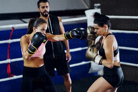 Female Boxers Sparring In The Ring Of A Boxing Club Watched By Trainer
