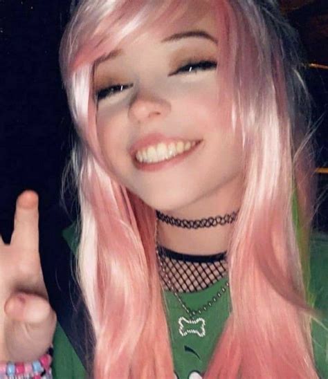 A Woman With Long Pink Hair Wearing A Green Shirt And Holding Up Her Peace Sign