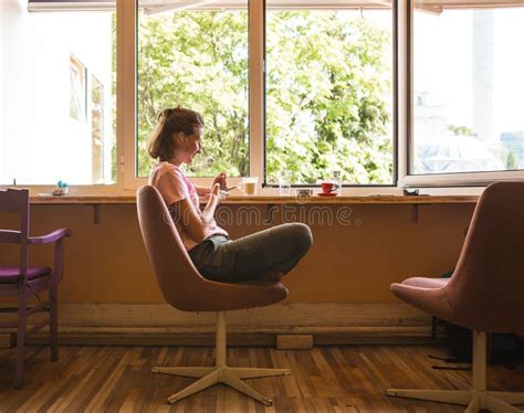 A Woman Is Sitting Near The Window And Drinking Coffee Stock Image