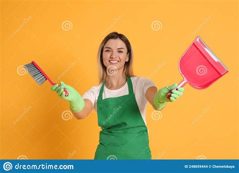 Young Woman With Broom And Dustpan On Orange Background Stock Photo